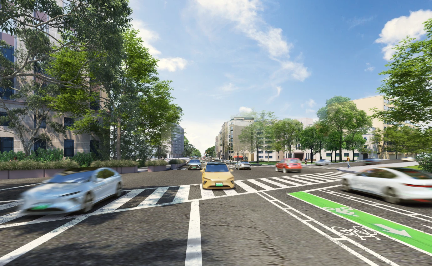 Wide urban intersection with bike lanes, moving cars, trees, and residential buildings on sunny day