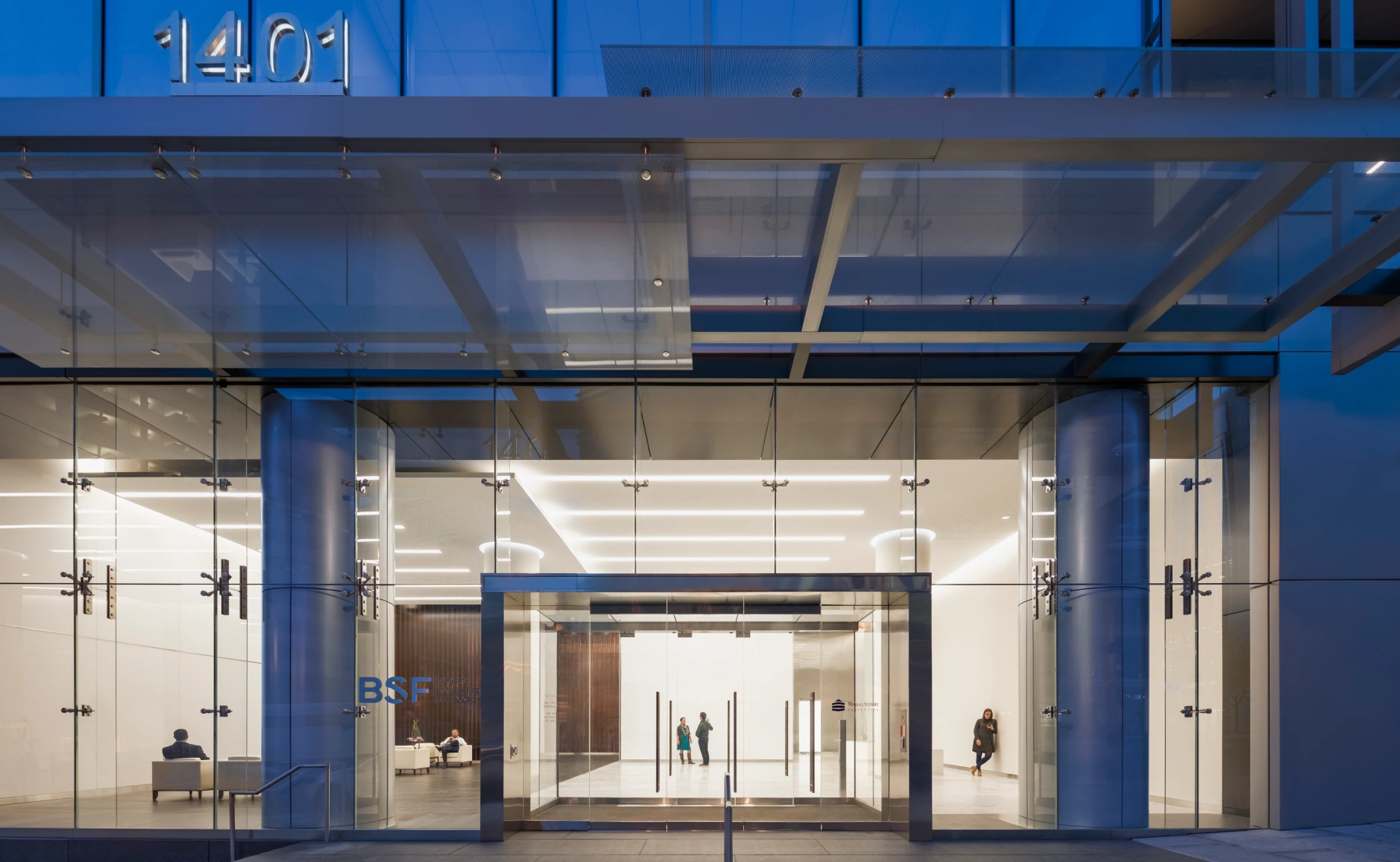 Contemporary commercial building exterior featuring glass canopy entryway and bright interior lighting