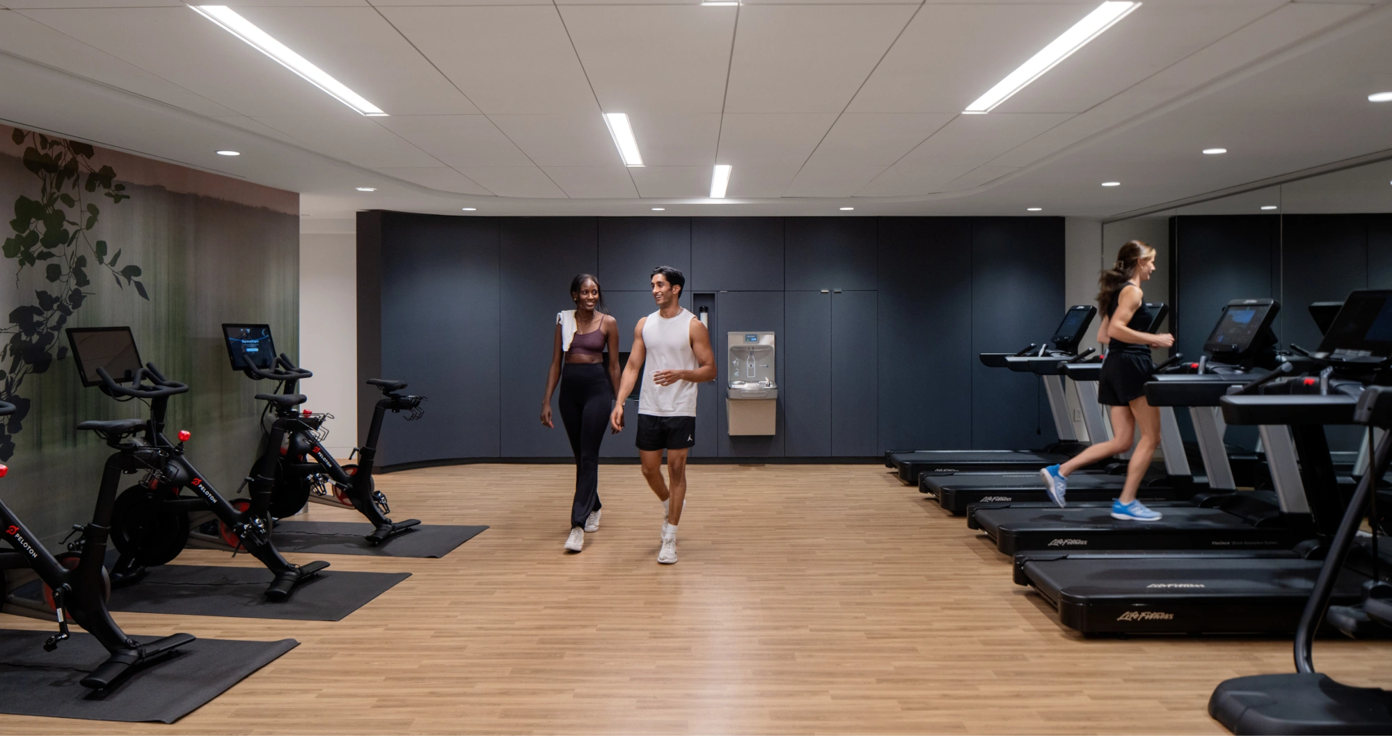 Modern apartment gym with treadmills, stationary bikes, and residents exercising in bright fitness room