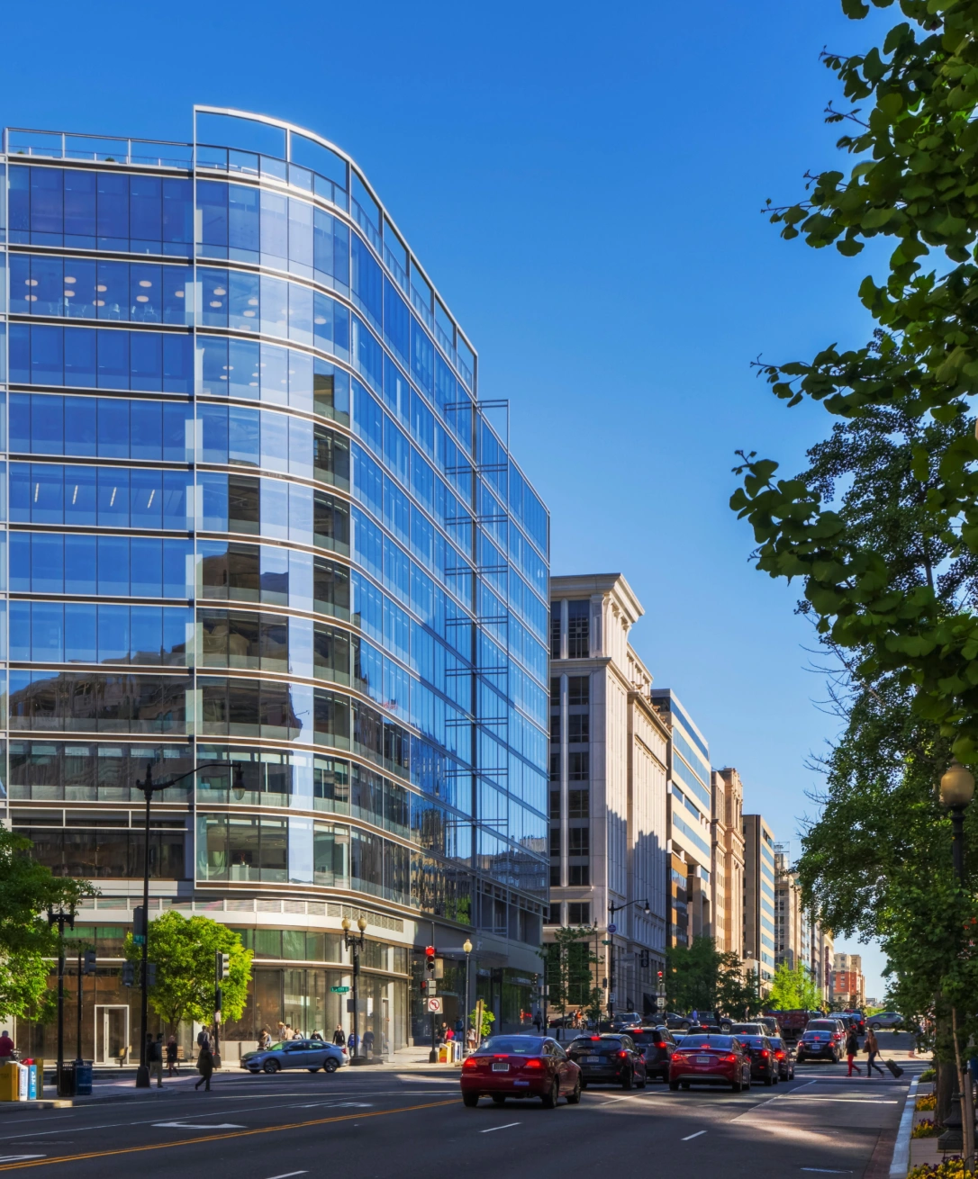 Contemporary commercial building with curved glass facade, urban streetscape, and surrounding office buildings