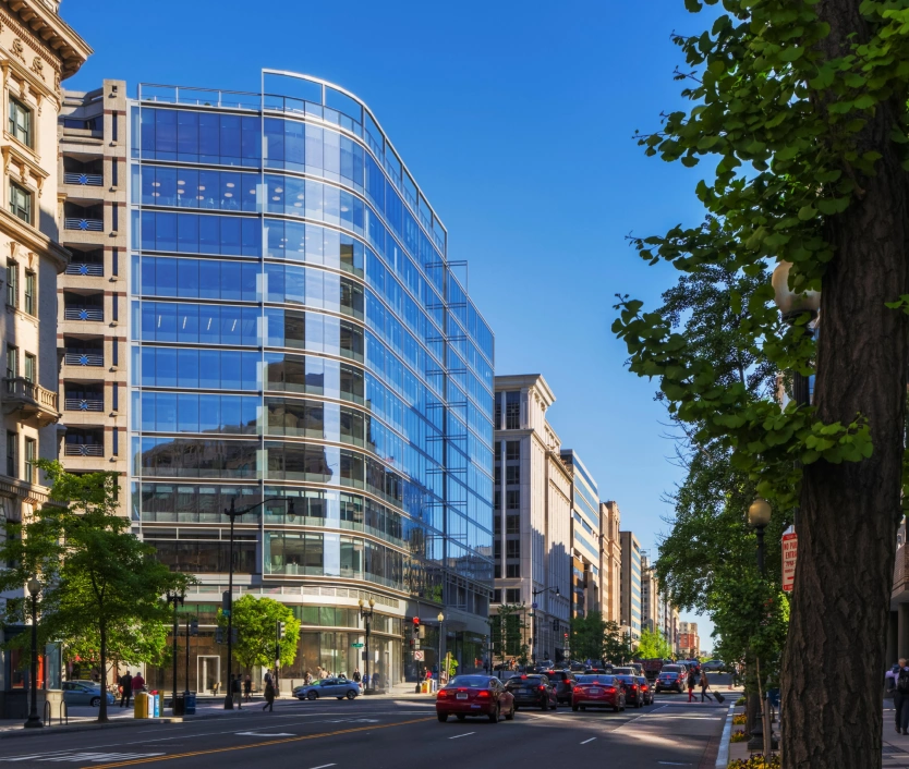 Contemporary urban office architecture featuring reflective glass exterior and tree-lined city avenue